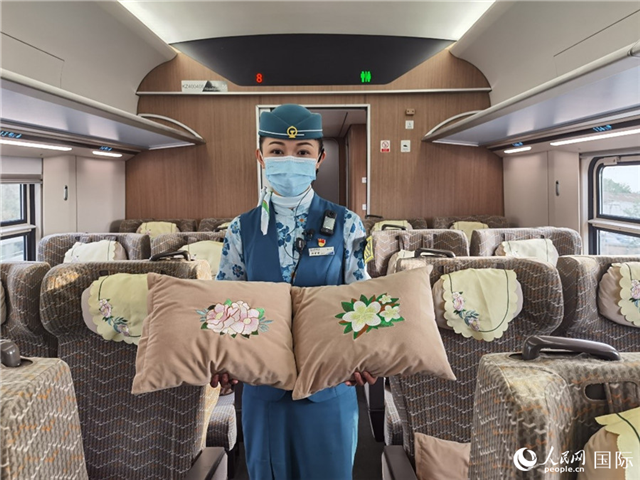 趙瑩靜展示中老鐵路國(guó)際旅客列車?yán)飵в兄袊?guó)牡丹花和老撾占巴花刺繡圖案的靠墊。人民網(wǎng)記者 杜明明攝