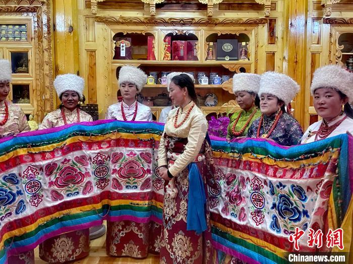 圖為女性展示村民自發(fā)繡制的“百米五彩哈達(dá)”?！±钣穹?攝